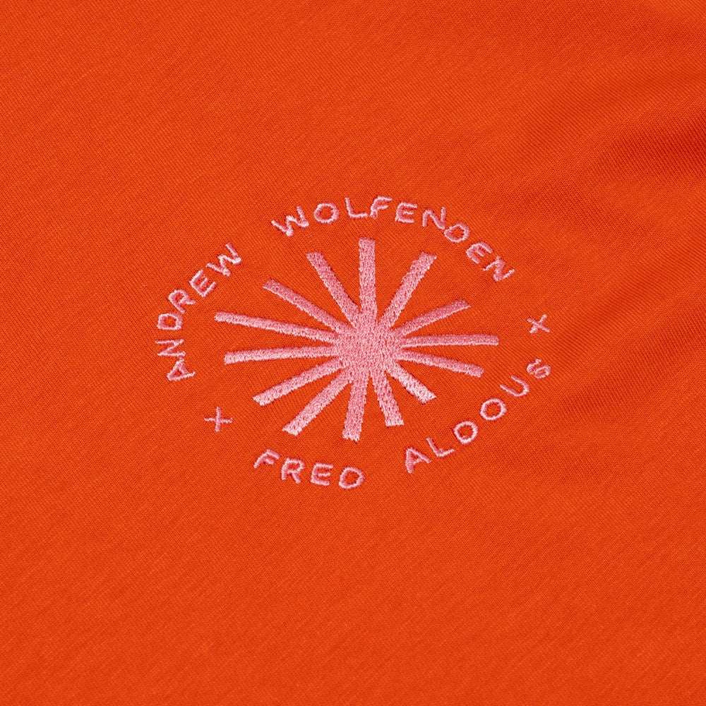 Embroidered logo on an orange fabric with 'Andrew Wolfenden' and 'Fred Aldous' text.