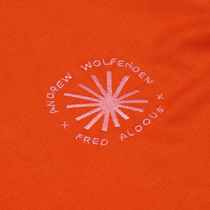 Embroidered logo on an orange fabric with 'Andrew Wolfenden' and 'Fred Aldous' text.