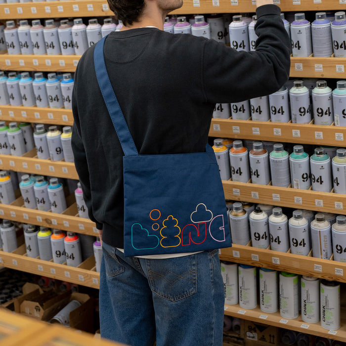 Person with a blue bag featuring colorful graphics in a store aisle with paint cans.